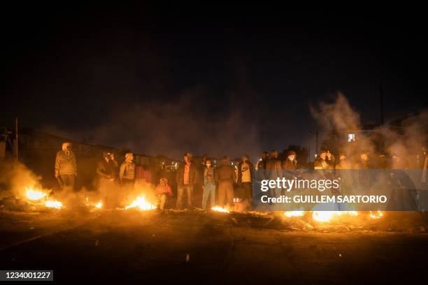 Armed community members gather around a fire to keep warm at a road block set up in Phoenix Township, North Durban, on July 15, 2021 to prevent...