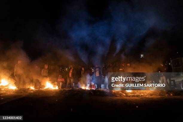 Armed community members gather around a fire to keep warm at a road block set up in Phoenix Township, North Durban, on July 15, 2021 to prevent...
