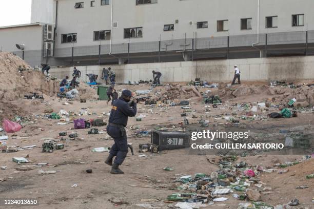 Member of SAPS shoots rubber bullets to disperse a crowd looting outside a warehouse storing alcohol in Durban on July 16 in the midst of an ongoing...