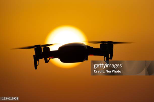 Quadcopter drone hovering during a flight in front of the sun. The flying drone is seen as a dark silhouette against the spectacular colorful sunset...