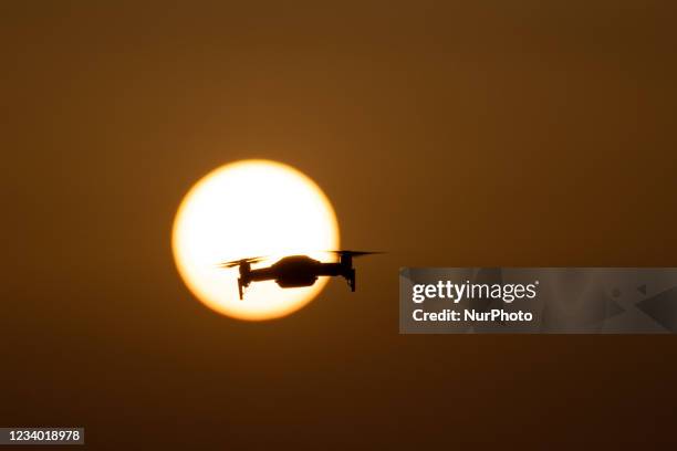 Quadcopter drone hovering during a flight in front of the sun. The flying drone is seen as a dark silhouette against the spectacular colorful sunset...