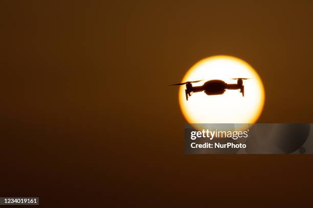 Quadcopter drone hovering during a flight in front of the sun. The flying drone is seen as a dark silhouette against the spectacular colorful sunset...