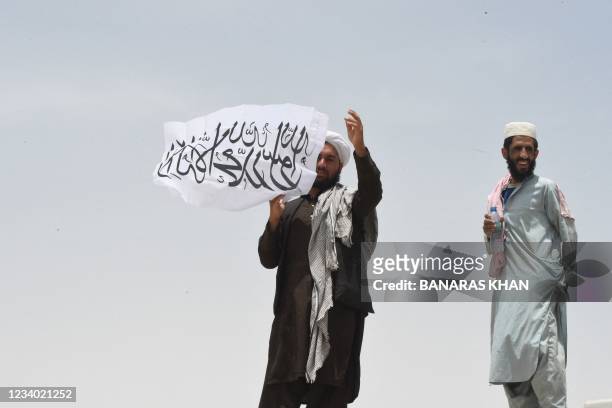 Man standing on Afghanistan's side of the border holds a Taliban flag as people walk towards a border crossing point in Pakistan's border town of...