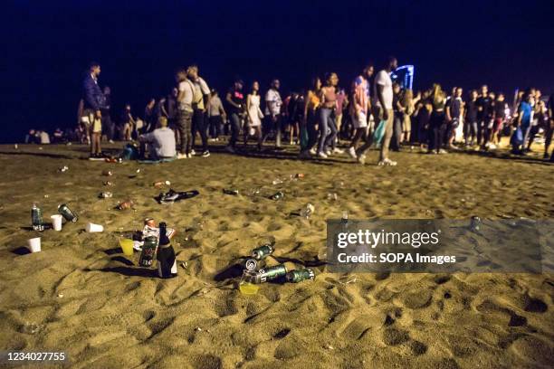 Cans and bottles of alcoholic beverages are seen on the sand of Barceloneta beach in front of a crowd of people. Police evicts crowds from...