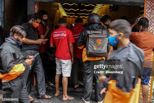 Delivery riders for Zomato Ltd., center, and Swiggy, operated by Bundl Technologies Pvt., wait to collect orders outside a restaurant in Mumbai,...