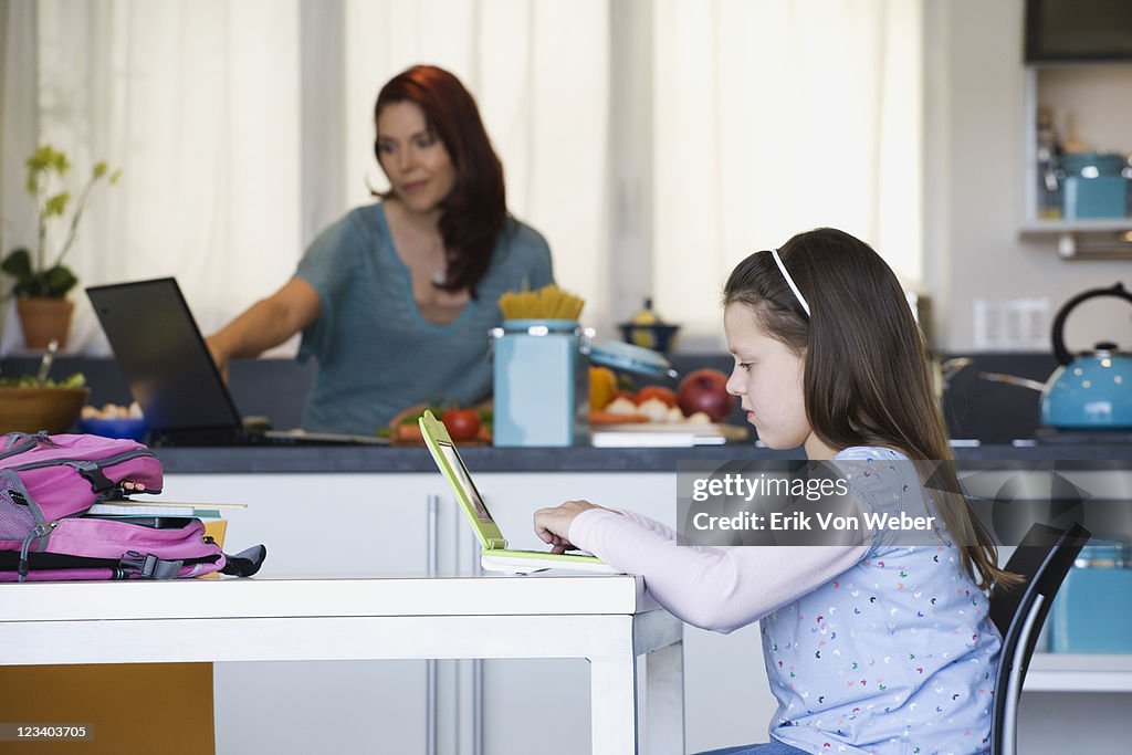 Mother and daughter in kitchen working on laptops