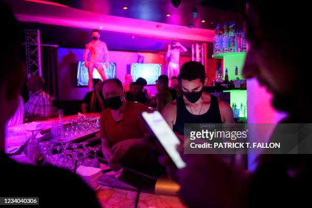 Employees wear face masks as people dance and drink at a nightclub after midnight early Sunday morning on July 18, 2021 in West Hollywood,...
