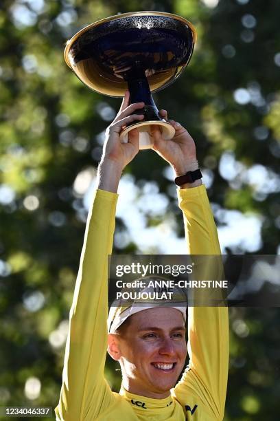 Winner Team UAE Emirates' Tadej Pogacar of Slovenia celebrates with the trophy wearing the overall leader yellow jersey on the podium at the end of...