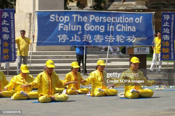 Banner demanding the Chinese government to stop Falun Gong seen behind Falun Gong practitioners meditating outside the Houses of Parliament during a...