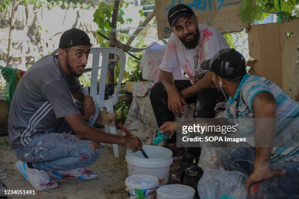 Palestinian artist, Belal Khaled and his team take a rest after making final touches to a graffiti painting on a building wall destroyed by Israeli...
