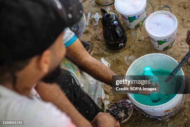 Palestinian artist, Belal Khaled and his team prepares paint before putting the final touches to a graffiti painting on a building wall destroyed by...