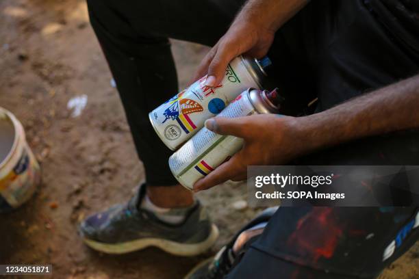 Palestinian artist, Belal Khaled holds spray paint before making final touches to a graffiti painting on a building wall destroyed by Israeli...