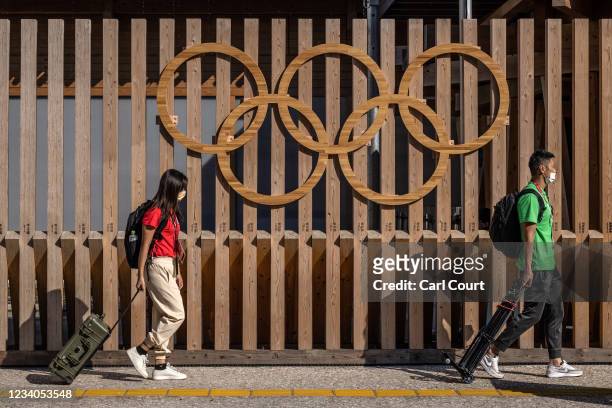 Foreign journalists carry broadcast equipment past Olympic Rings as they walk to the media centre at Tokyo Olympics athletes village on July 19, 2021...