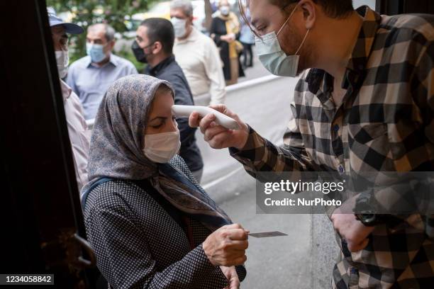 An official takes the body temperature measurement of an Iranian woman as she arrives a sport hall for receiving a dose of the China's Sinopharm new...