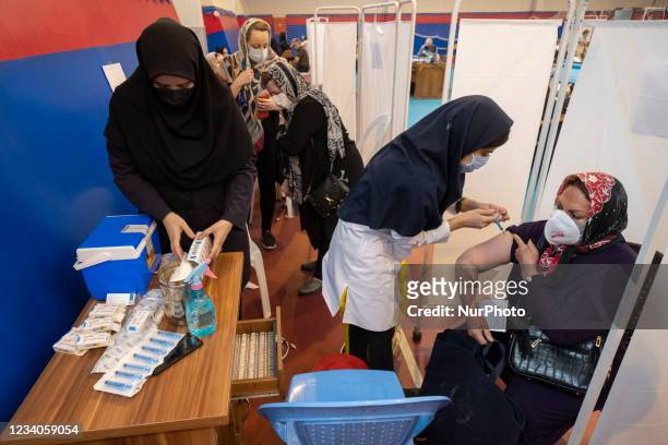 An Iranian woman wearing a protective face mask receives a dose of China's Sinopharm new coronavirus disease vaccine, at a sports hall during general...