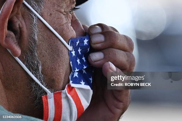 Man adjusts his American flag face mask on July 19, 2021 on a street in Hollywood, California, on the second day of the return of the indoor mask...