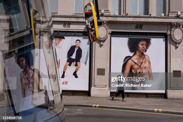 Reflected in the windscreen of a London bus, a shopper walks beneath advertising billboards for fashion retailer H&M in the West End on Covid...