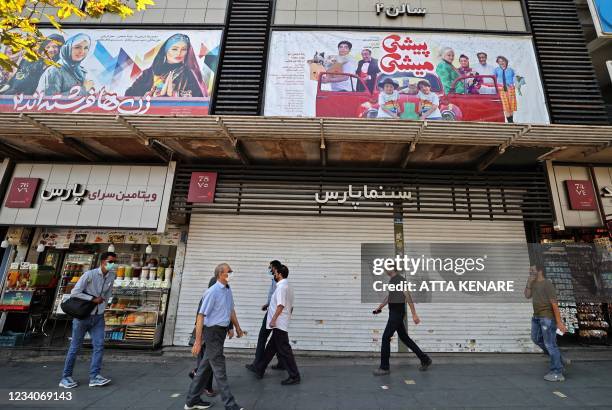 Iranians walk past a shuttered cinema hall in downtown Tehran on July 20, 2021. - Iran a day earlier announced strict curbs in the capital Tehran and...
