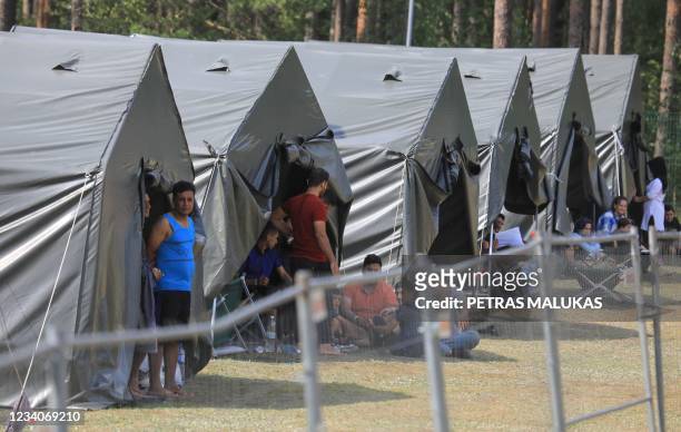 Migrants are seen through a fence as they stand and sit by tents in a camp near the border town of Kapciamiestis, Lithuania, on July 18, 2021. -...