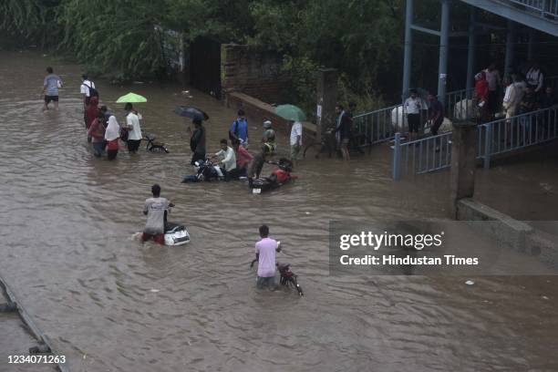 Commuters wade through a waterlogged road due to heavy rains, near Narsingh pur, on July 19, 2021 in New Delhi, India.