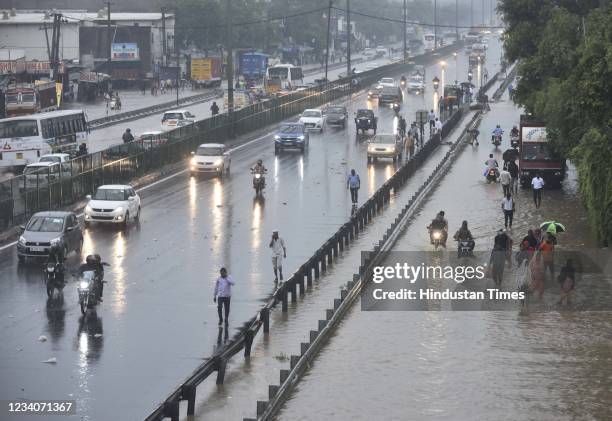 Commuters wade through a waterlogged road due to heavy rains, near Narsingh pur, on July 19, 2021 in New Delhi, India.