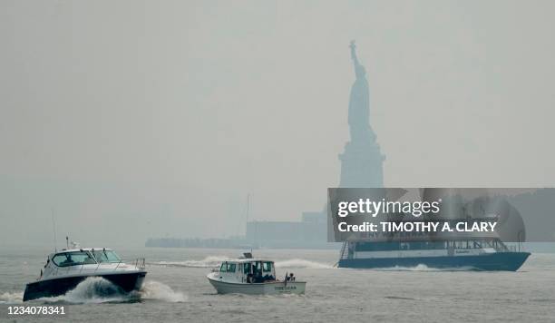 Boats pass by a hazy Statue of Liberty, seen from Exchange Place in Jersey City, New Jersey on July 20, 2021 as New York officials issue a air...