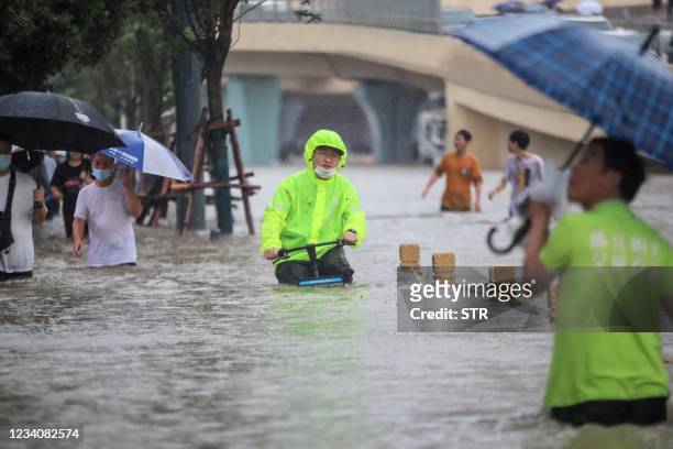 This photo taken on July 20, 2021 shows a man riding a bicycle through flood waters along a street following heavy rains in Zhengzhou in China's...