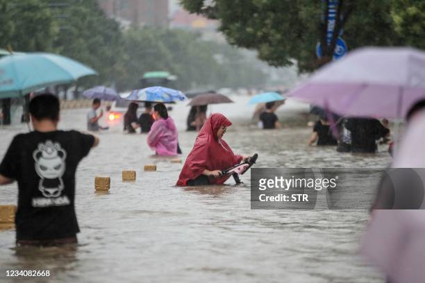 This photo taken on July 20, 2021 shows people wading through flood waters along a street following heavy rains in Zhengzhou in China's central Henan...