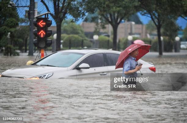 This photo taken on July 20, 2021 shows a man wading past a submerged car along a flooded street following heavy rains in Zhengzhou in China's...