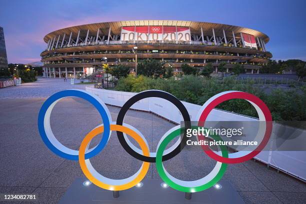 July 2021, Japan, Tokio: In the evening twilight Olympic rings stand in front of the Olympic Stadium. The Olympic Stadium is the sports venue of the...