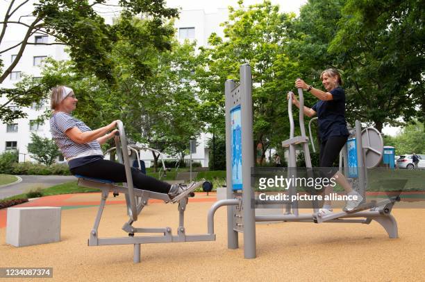 July 2021, Saxony, Dresden: Maria Jungrichter and Hannelore Bernhardt stand or sit on fitness equipment in front of a residential building with...