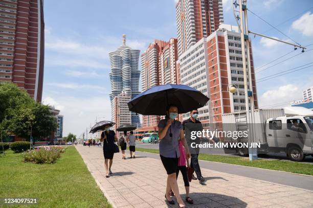 People shelter beneath umbrellas as they walk along Mirae Street during temperatures of 34 degrees celsius, in Pyongyang on July 21, 2021.