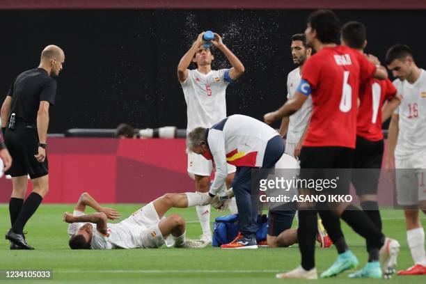 Spain's midfielder Dani Ceballos gets treatment for an injury as Spain's defender Jesus Vallejo sprays himself during the Tokyo 2020 Olympic Games...