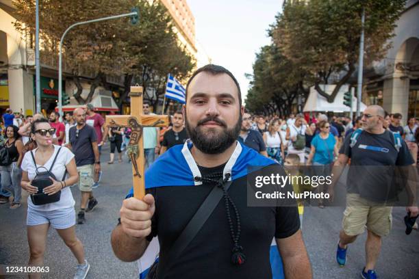 Young male protester is holding a cross with Jesus and carrying the Greek Flag during the Demonstration Against The Mandatory Vaccine was held in...