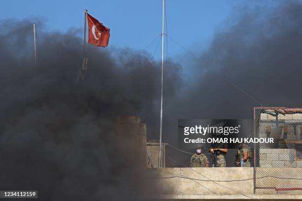 Turkish soldiers stand guard atop an outpost as smoke billows from burning tyres during a demonstration against Turkey's perceived inaction over the...