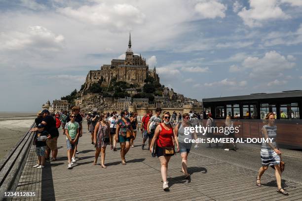 Tourists walk in front of the Mont-Saint-Michel, in Normandy, northwestern France, on July 22, 2021. - French cinemas, museums and sports venues...