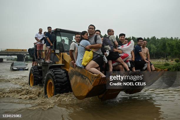 People ride the front of a wheel loader to cross a flooded street following heavy rains which caused flooding and claimed the lives of at least 33...