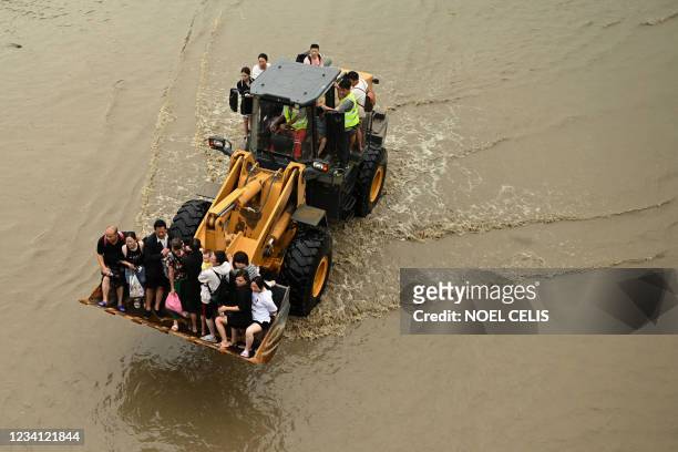 People ride in the front of a wheel loader down a flooded street following heavy rains which caused flooding and claimed the lives of at least 33...