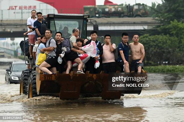 People ride in the front of a wheel loader to cross a flooded street following heavy rains which caused flooding and claimed the lives of at least 33...