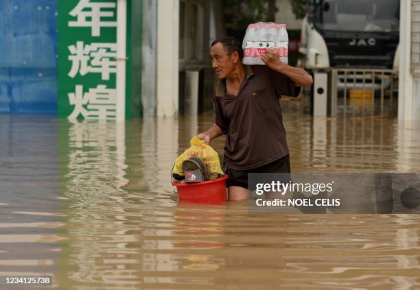Man carries bottled water as he cross a flooded street following heavy rain that flooded and claimed the lives of at least 33 people earlier in the...