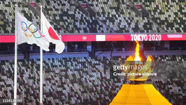 July 2021, Japan, Tokio: Olympia: Opening ceremony in the Olympic Stadium. The Olympic fire burns next to it the Olympic and Japanese flag. Photo:...