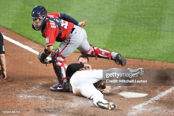 Trey Mancini of the Baltimore Orioles slides under Tres Barrera of the Washington Nationals on a fielders choice by Ramon Urias in the sixth inning...
