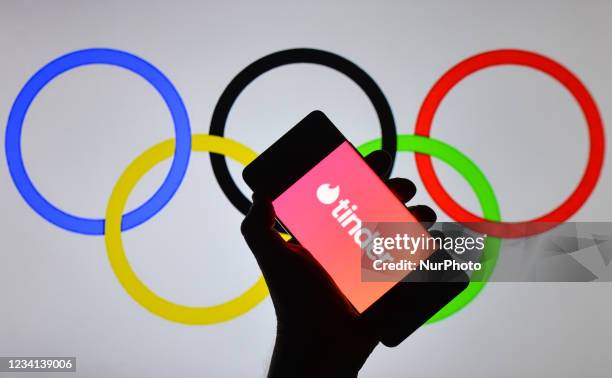 An illustrative image of the Tinder logo displayed on a mobile phone in front of Olympic Rings displayed on a screen. On Saturday, 24 July 2021, in...