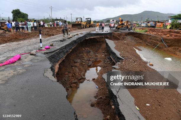 People gather along a section of highway partially washed away from the rain at Mahad on July 24 as the death toll from heavy monsoon rains climbed...