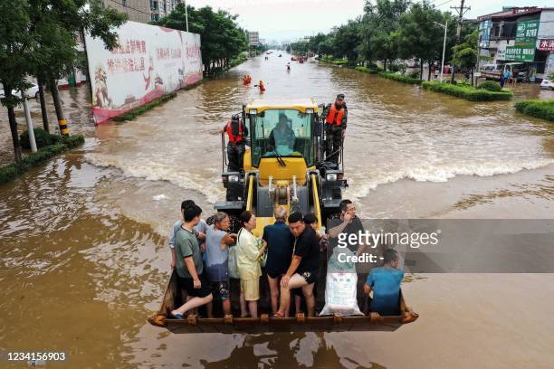 This aerial photo taken on July 23, 2021 shows residents riding in front of a loader to cross a flooded street following heavy rains in Xinxiang, in...