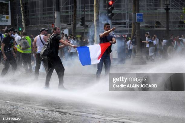 Protesters hold a French flag as they are water spead by police water trucks during a demonstration against the compulsory vaccination for certain...