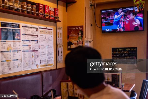 People watch a TV live broadcast of the Tokyo 2020 Olympic Games table tennis mixed doubles quarterfinals match between Japan's Jun Mizutani and Mima...