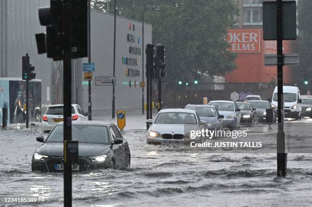 Cars drive through deep water on a flooded road in The Nine Elms district of London on July 25, 2021 during heavy rain. - Buses and cars were left...