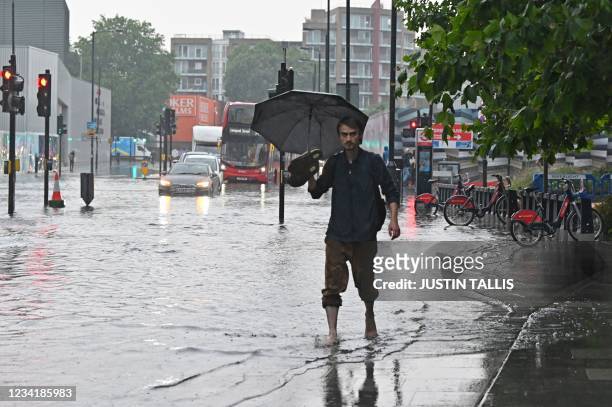 Pedestrian walks bare-footed along a flooded road in The Nine Elms district of London on July 25, 2021 during heavy rain. - Buses and cars were left...