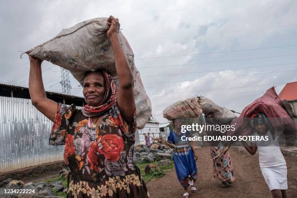 Internally displaced people carry sacks of branches over their heads at a camp in the town of Azezo, Ethiopia, on July 12, 2021. - The July 13...